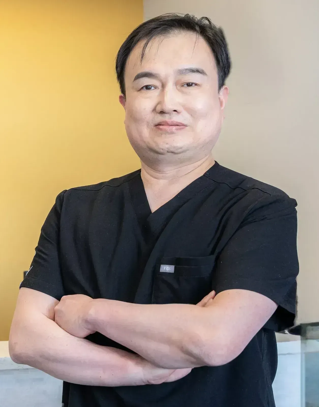 Man in black scrubs standing arms crossed beside 