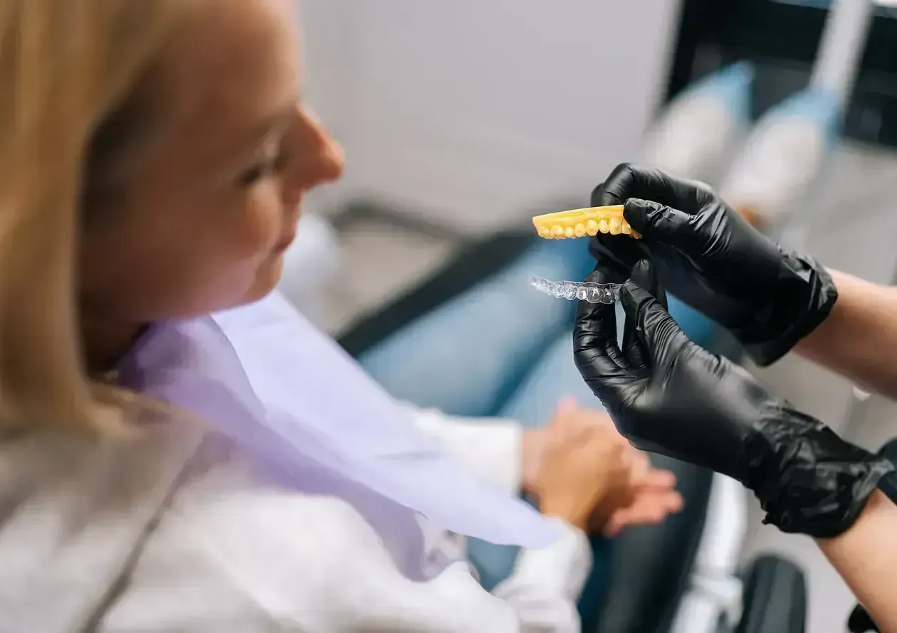 Woman smiling while holding a clear Invisalign aligner at Smiles of Niles family dentistry