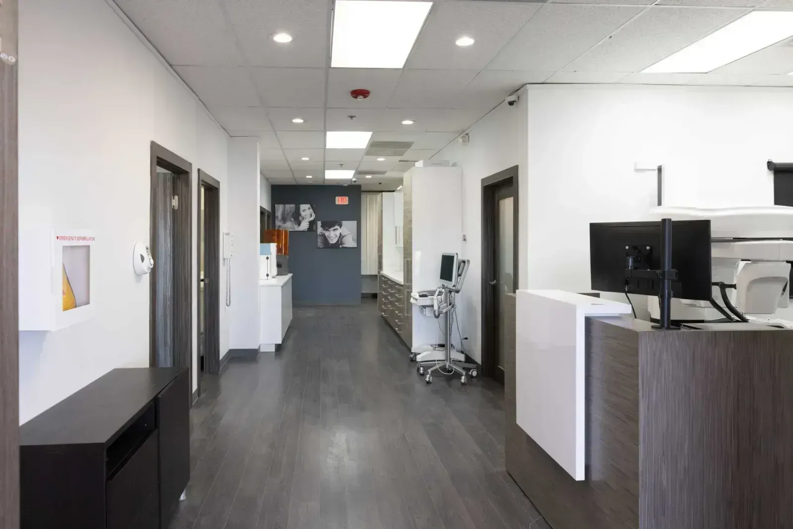 Modern dental office hallway with medical equipment, monitors, and defibrillator cabinet.