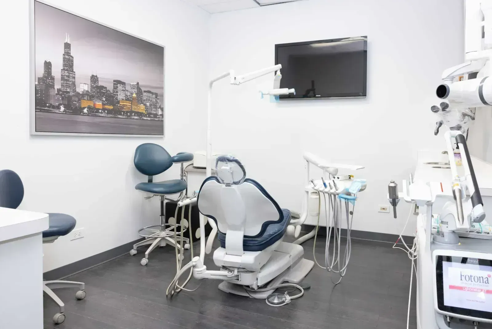 Modern dental treatment room with reclined chair, equipment tray, and Chicago skyline artwork.